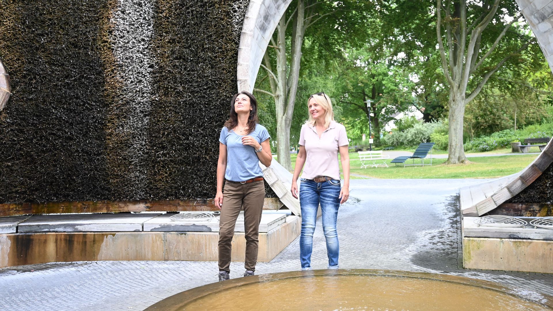 Twee lachende vrouwen wandelen door een paviljoen met afstudeertoren in het park.