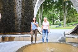 Twee lachende vrouwen wandelen door een paviljoen met afstudeertoren in het park.