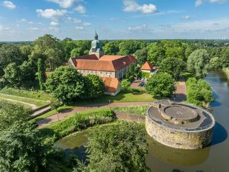 Historisch kasteel omringd door weelderig groen landschap met slotgracht en ronde toren op de voorgrond.