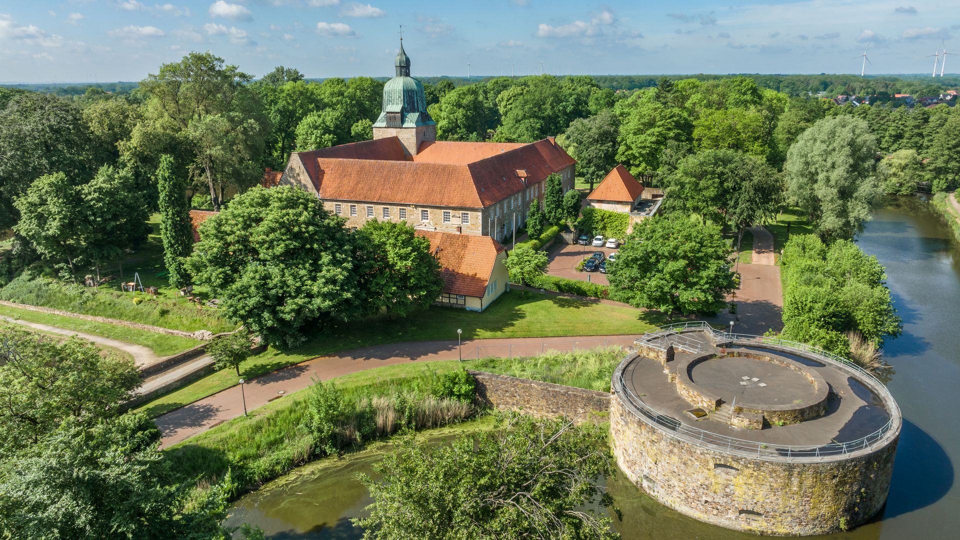 Historisch kasteel omringd door weelderig groen landschap met slotgracht en ronde toren op de voorgrond.