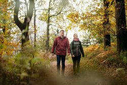 Zwei Personen spazieren fröhlich durch einen herbstlichen Waldpfad in buntem Laub.