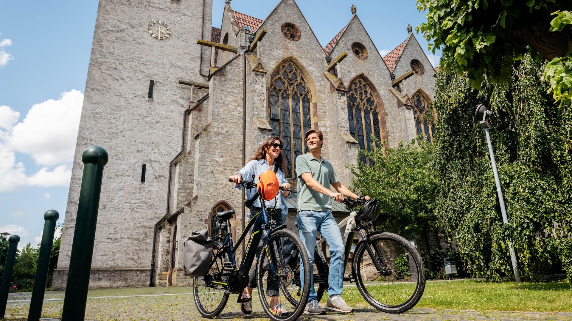 Twee mensen op de fiets voor een historische kerk met gotische ramen.