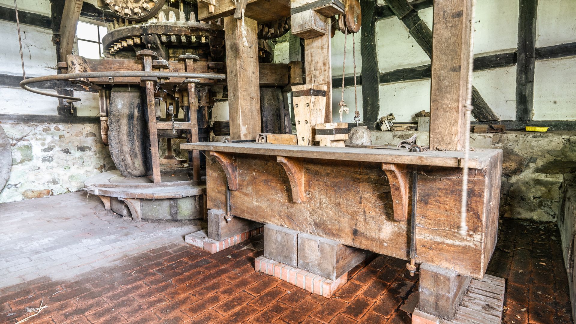 Alte Wassermühle mit hölzernen Zahnrädern und robustem Holzbalken in rustikalem Raum.