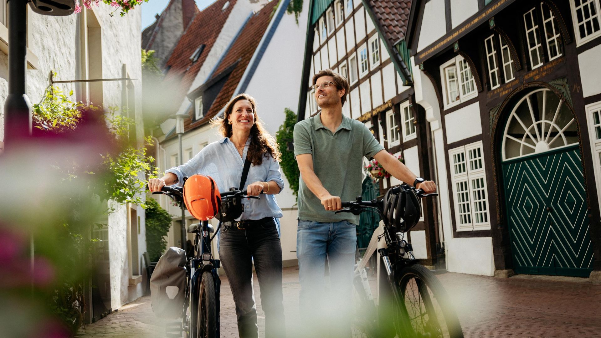 Twee mensen lopen met fietsen door een geplaveide straat met vakwerkhuizen.