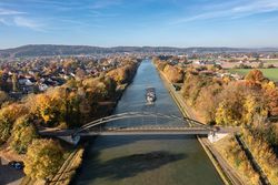 Brug over een herfstige rivier met een vrachtschip, omringd door kleurrijk gebladerte.