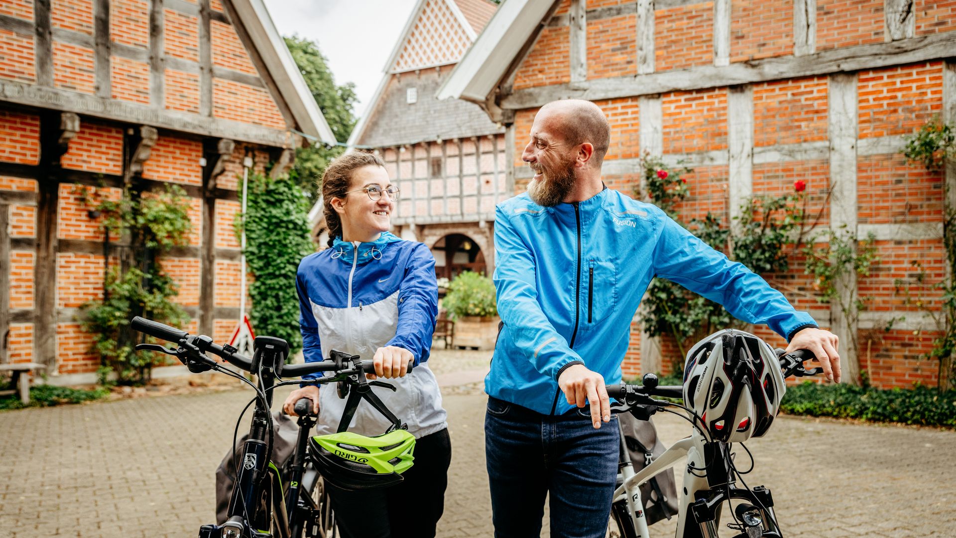 Lachend stel met fietsen voor historische vakwerkhuizen in een landelijke omgeving.
