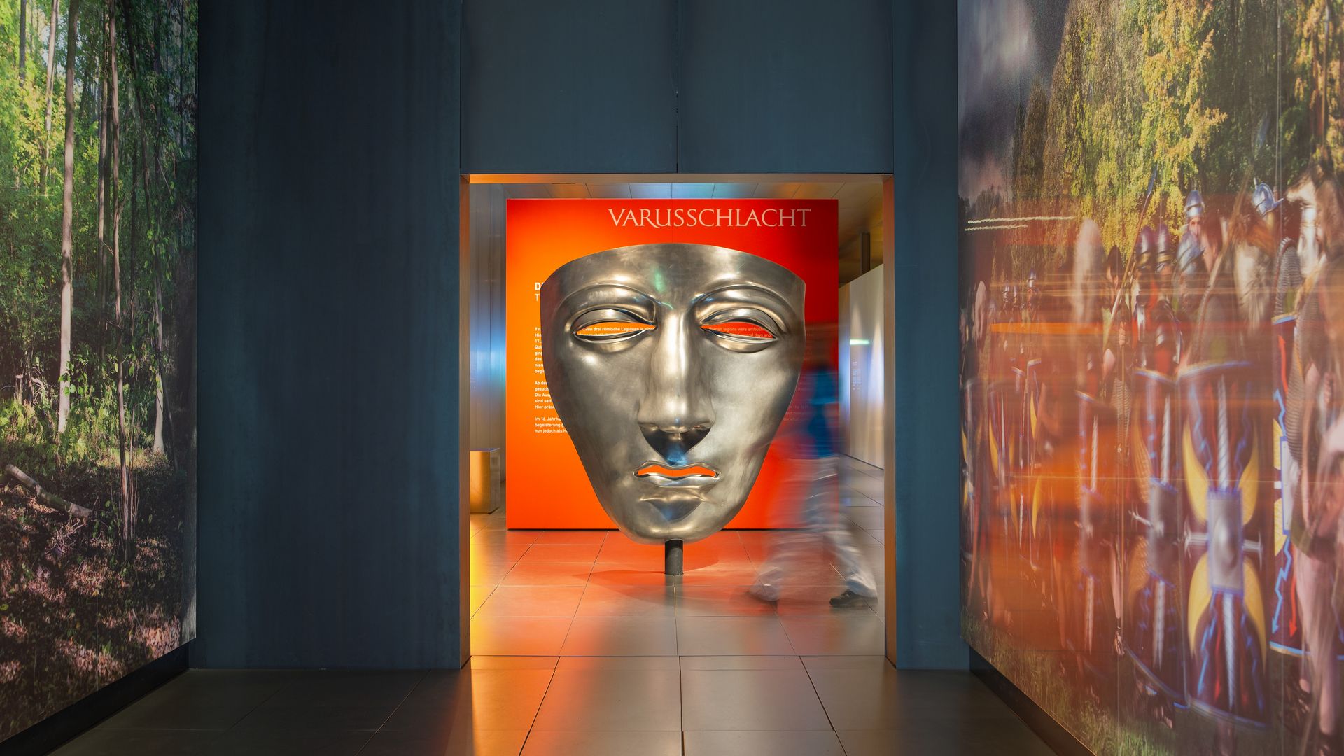 Groot zilveren masker in het Varusslagmuseum met bezoekers in de gang.