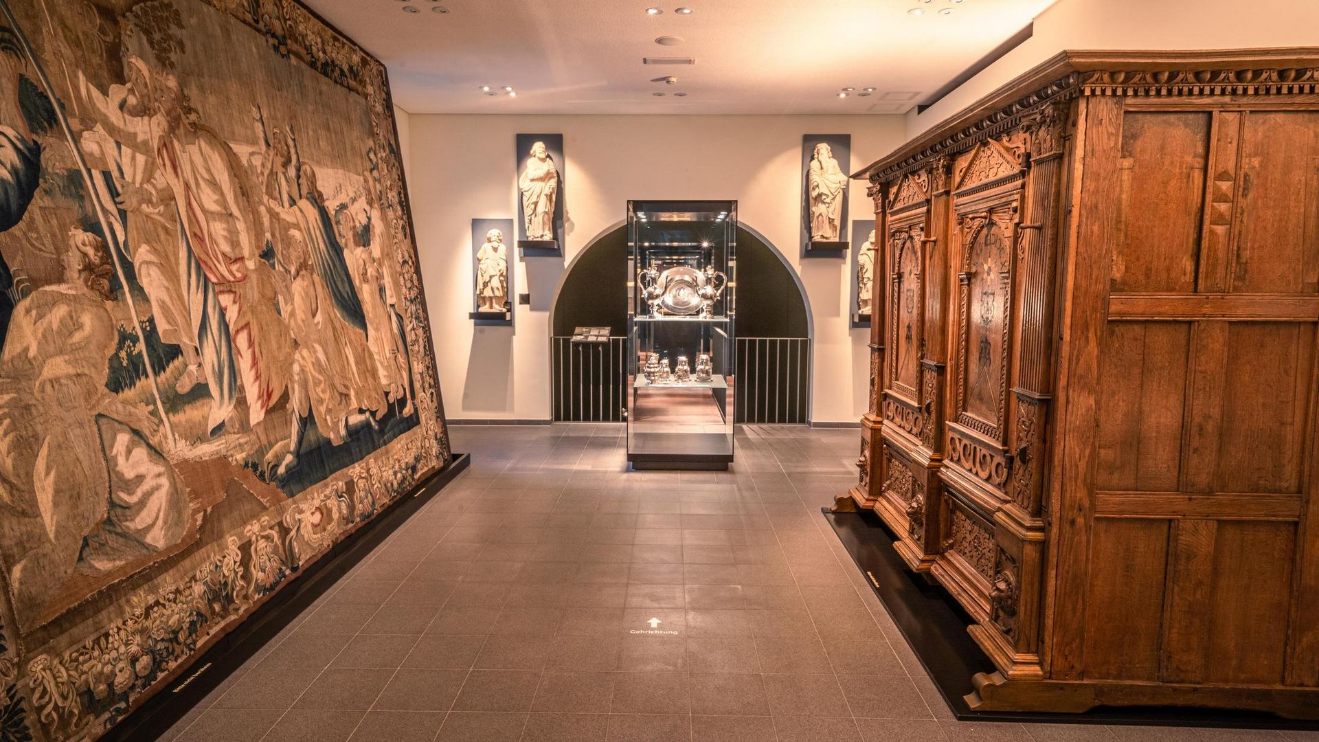 Tentoonstellingsruimte in het Diocesaan Museum Osnabrück met beelden, waardevol wandtapijt en houten kast.