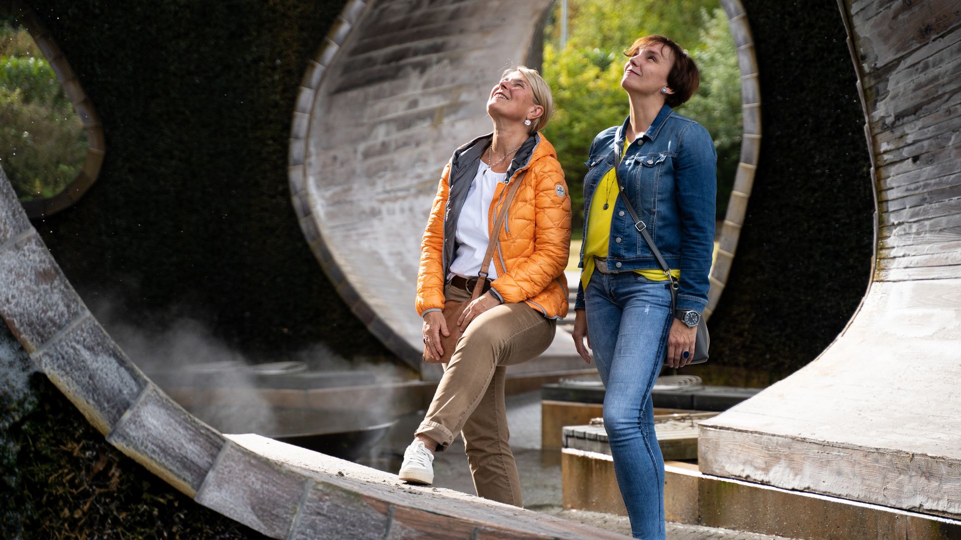 Twee vrouwen genieten bij zonnig weer van een kunstzinnig beeldhouwwerk in de open lucht.
