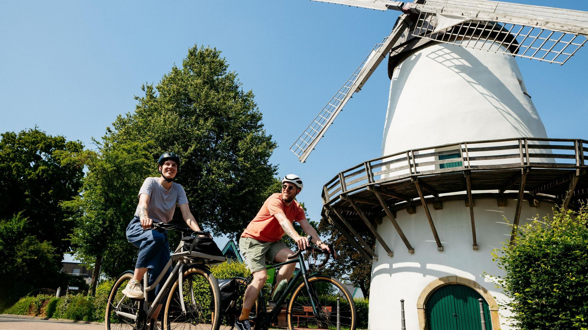 Twee fietsers voor een historische molen bij zonnig weer.