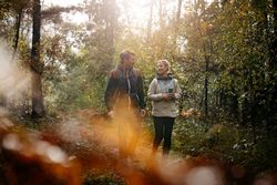 Twee mensen wandelen in een zonovergoten bos in herfstsfeer.