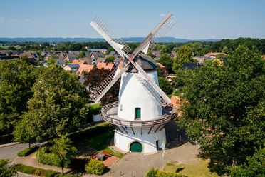 Windmolen met draaiende wieken omringd door groen landschap en kleine huizen.