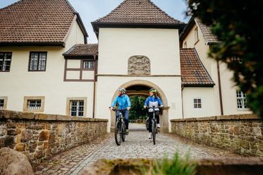 Twee fietsers passeren een historisch poortgebouw op kasseien.