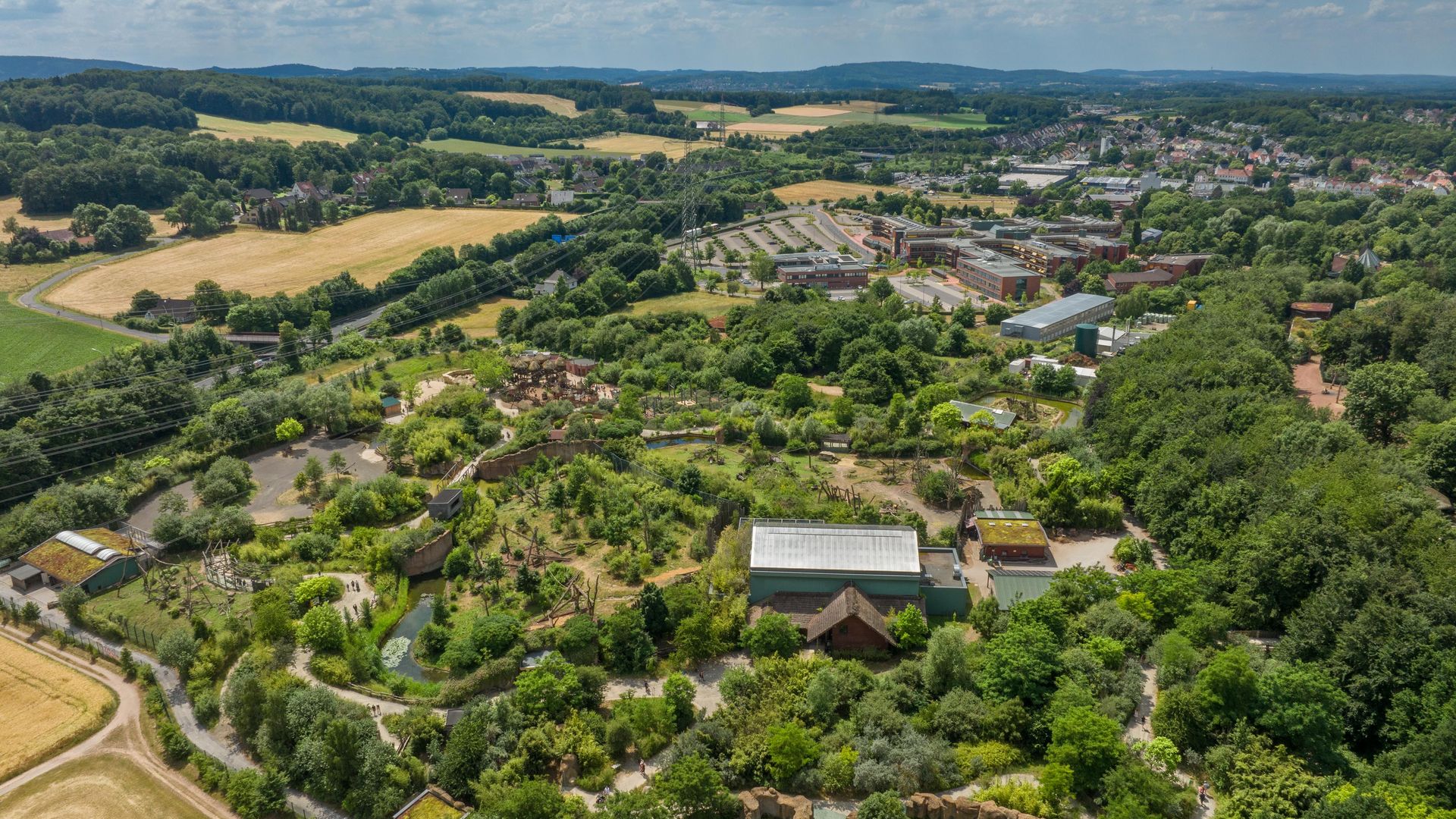 Luchtfoto van een uitgestrekt, groen landschap met gebouwen en velden op de achtergrond.