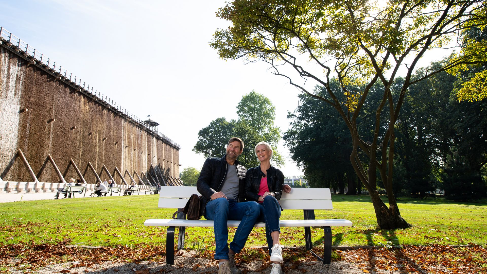 Een stel zit ontspannen op een bankje in het park voor een afstudeermuur op een zonnige dag.