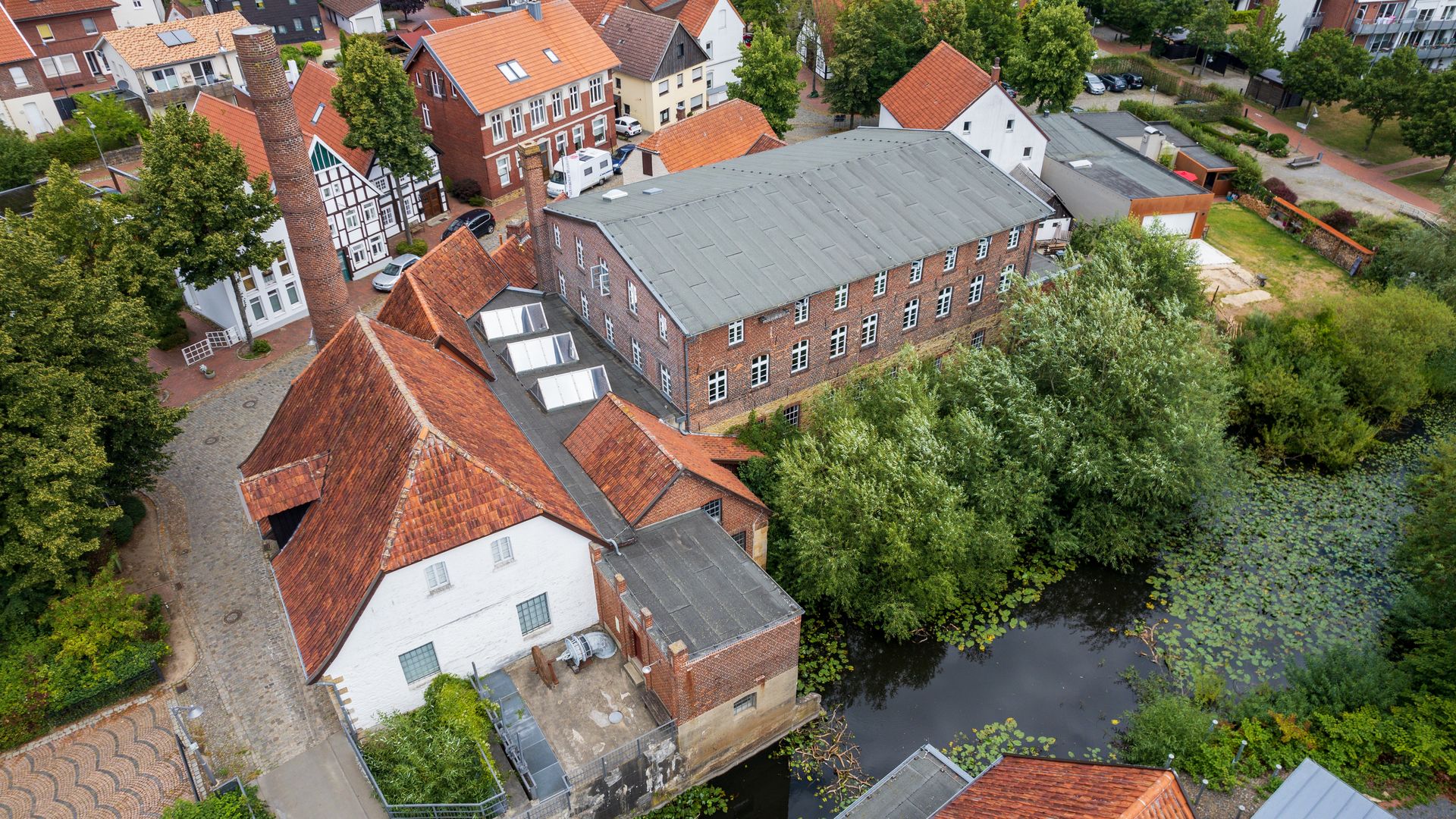Historische Ziegelgebäude mit roten Dächern neben einem Teich voller Seerosen.