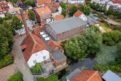 Historische Ziegelgebäude mit roten Dächern neben einem Teich voller Seerosen.