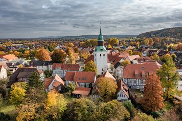 Luchtfoto van een dorp met historische kerktoren, vakwerkhuizen en herfstbladeren.