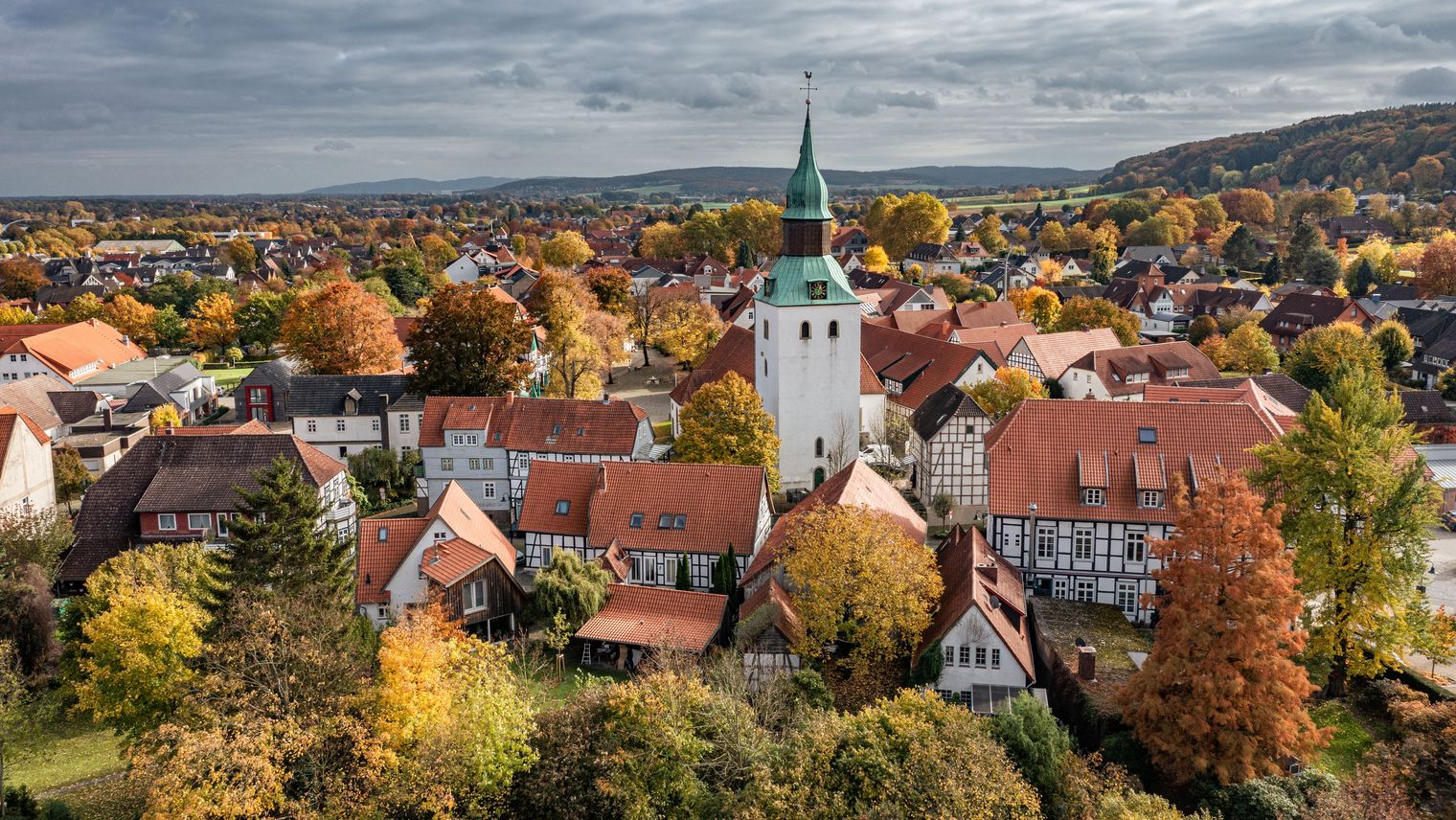 Luchtfoto van een dorp met historische kerktoren, vakwerkhuizen en herfstbladeren.