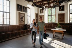 Ein Paar betrachtet historische Gemälde in einem holzvertäfelten Raum mit viel Tageslicht.